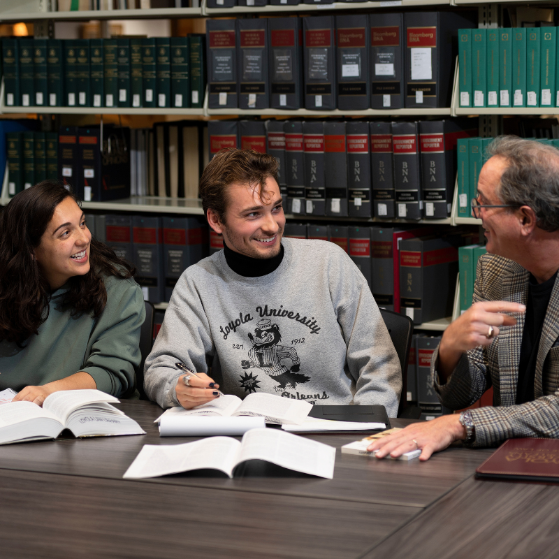 Two students studying in the library with a professor.