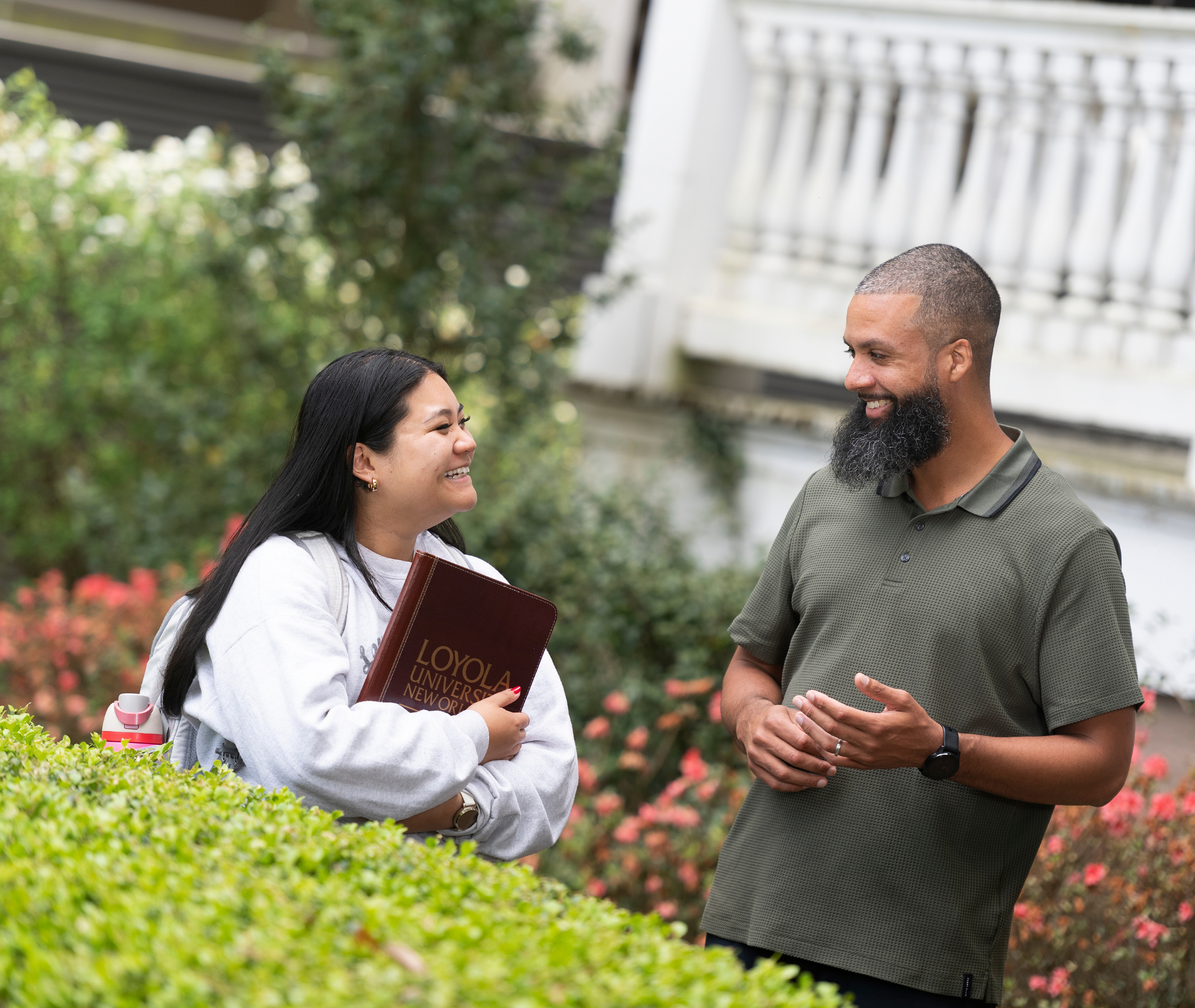 A student smiles and holds a Loyola University New Orleans padfolio while talking to a professor.