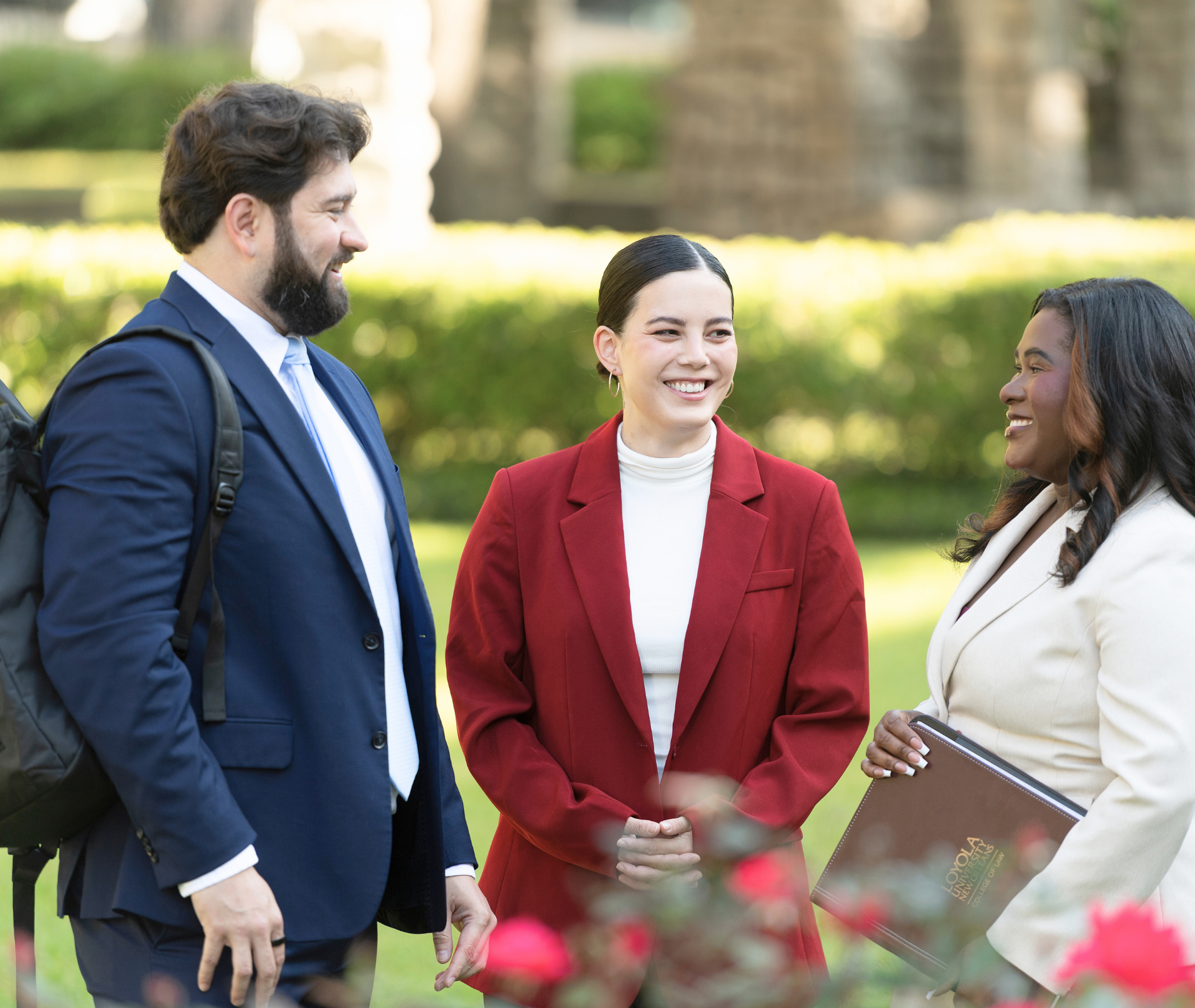 Three students in business clothes smiling outdoors.